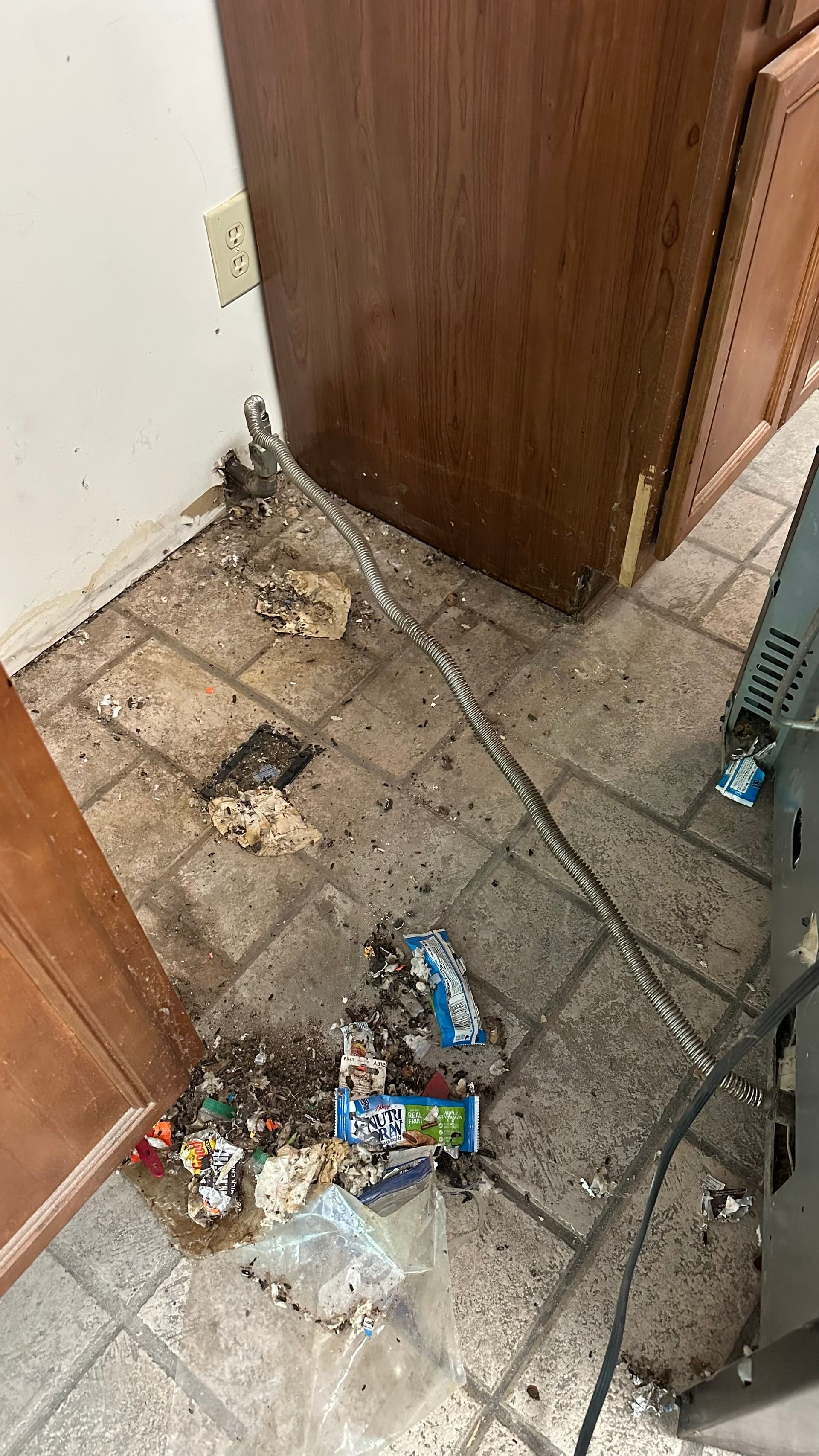 Debris on a tiled floor behind an appliance before a move-out clean